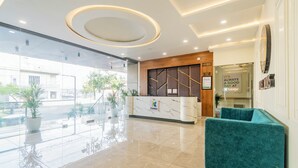 A modern reception area with a marble counter, a clock, and a teal sofa. - Treebo Indus (Jaipur)