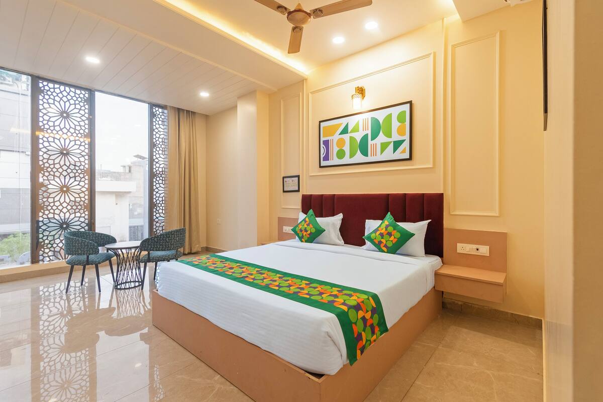 A hotel room with a bed, a ceiling fan, a window with a view, and a small table with chairs.
