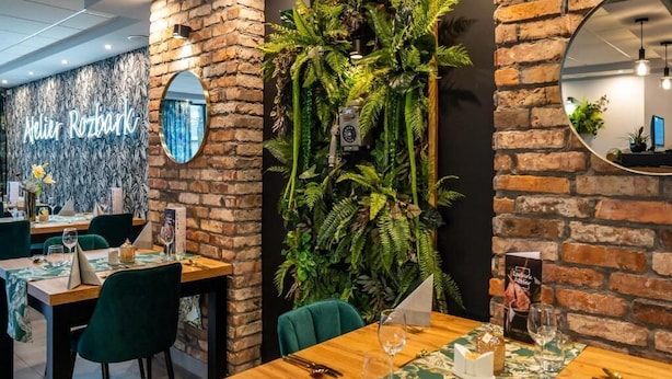 L’intérieur d’un restaurant avec des murs en briques, des chaises vertes et une composition végétale fixée au mur.