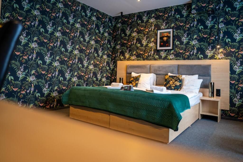 Un dormitorio con cama, mesitas de noche, un cuadro enmarcado en la pared y un estampado floral en el papel tapiz.