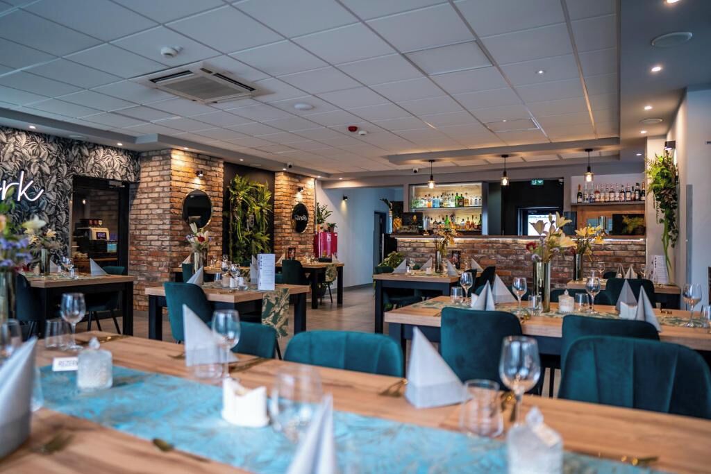 Un restaurante con pared de ladrillo, mesas de madera y sillas verdes.