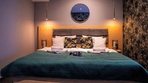 Un lit bien fait, recouvert d’une couverture verte, avec deux oreillers et un miroir rond accroché au mur.