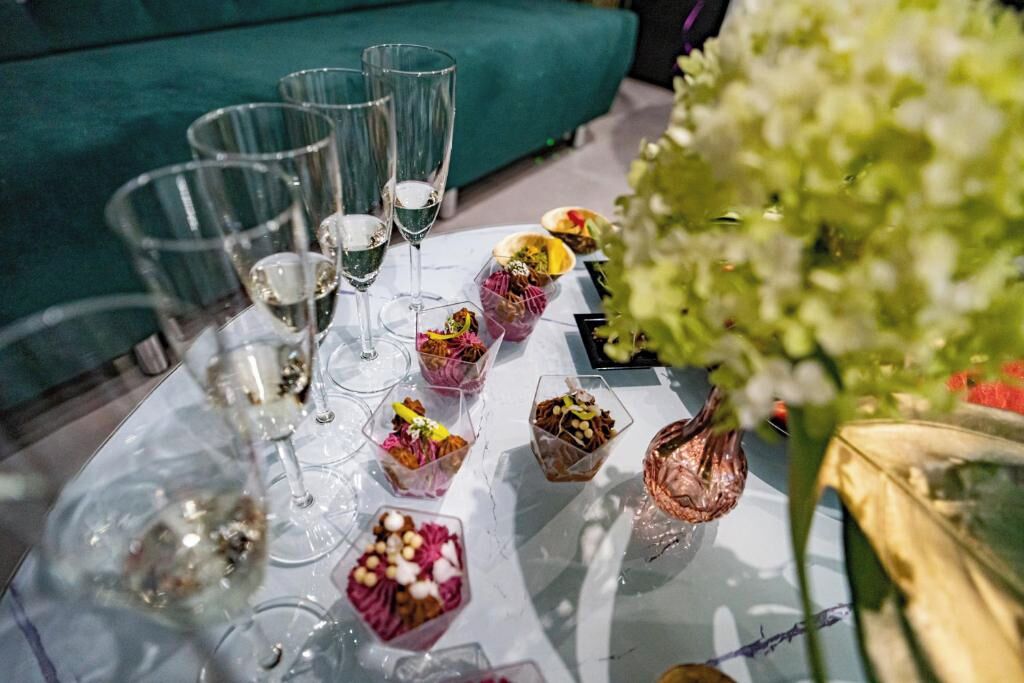 Una mesa con vasos transparentes, copas para postres pequeños y un arreglo floral verde.