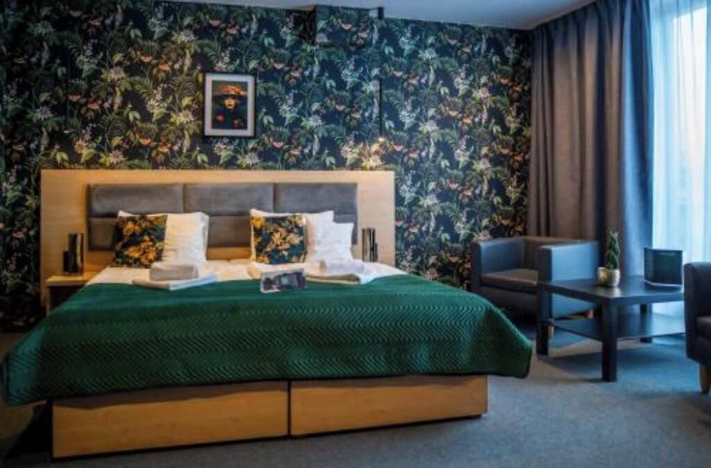 Una habitación de hotel con una cama, una silla, una mesita y una pared con estampado floral.