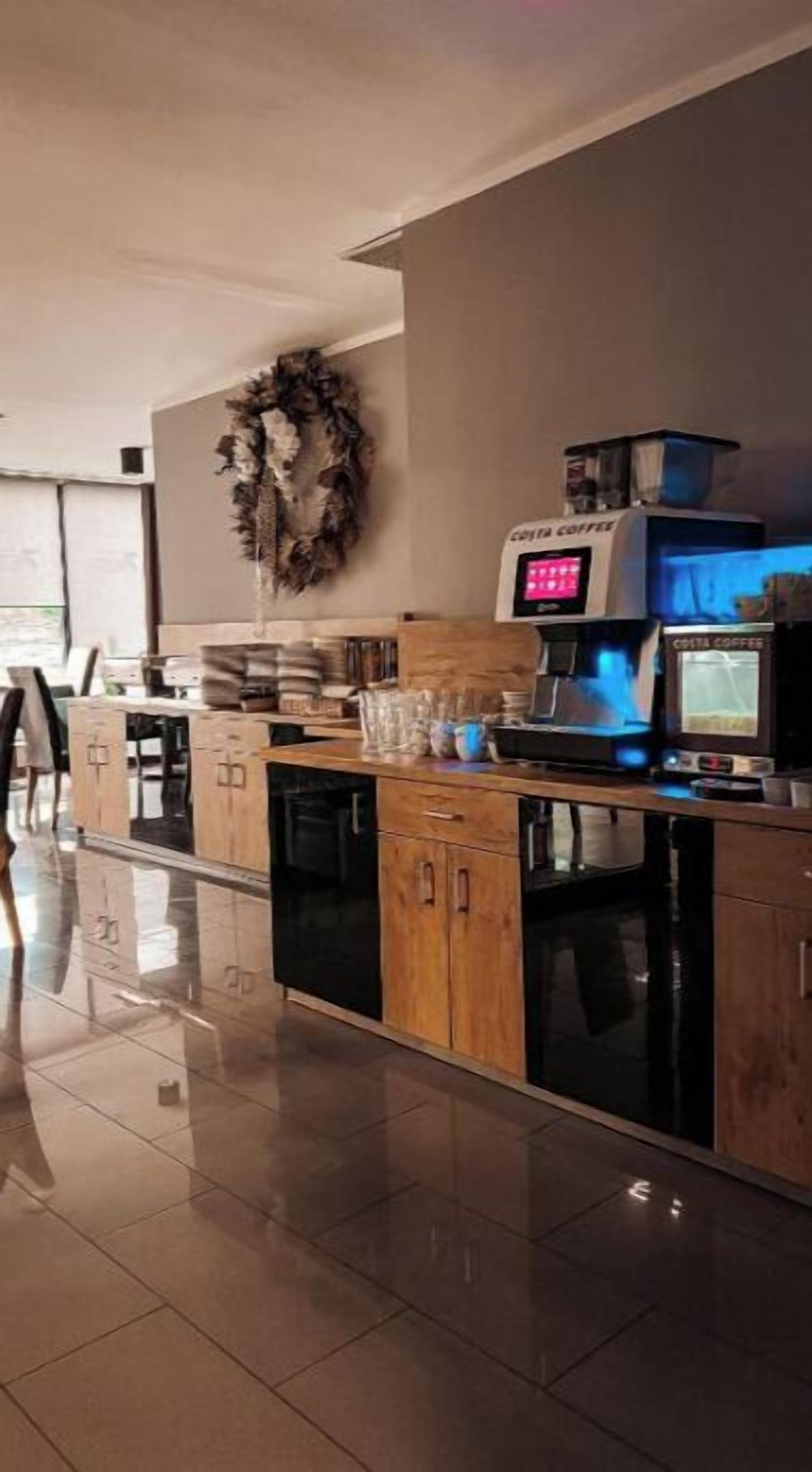 A modern kitchen with wooden cabinets, a coffee machine, and a decorative wreath on the wall.