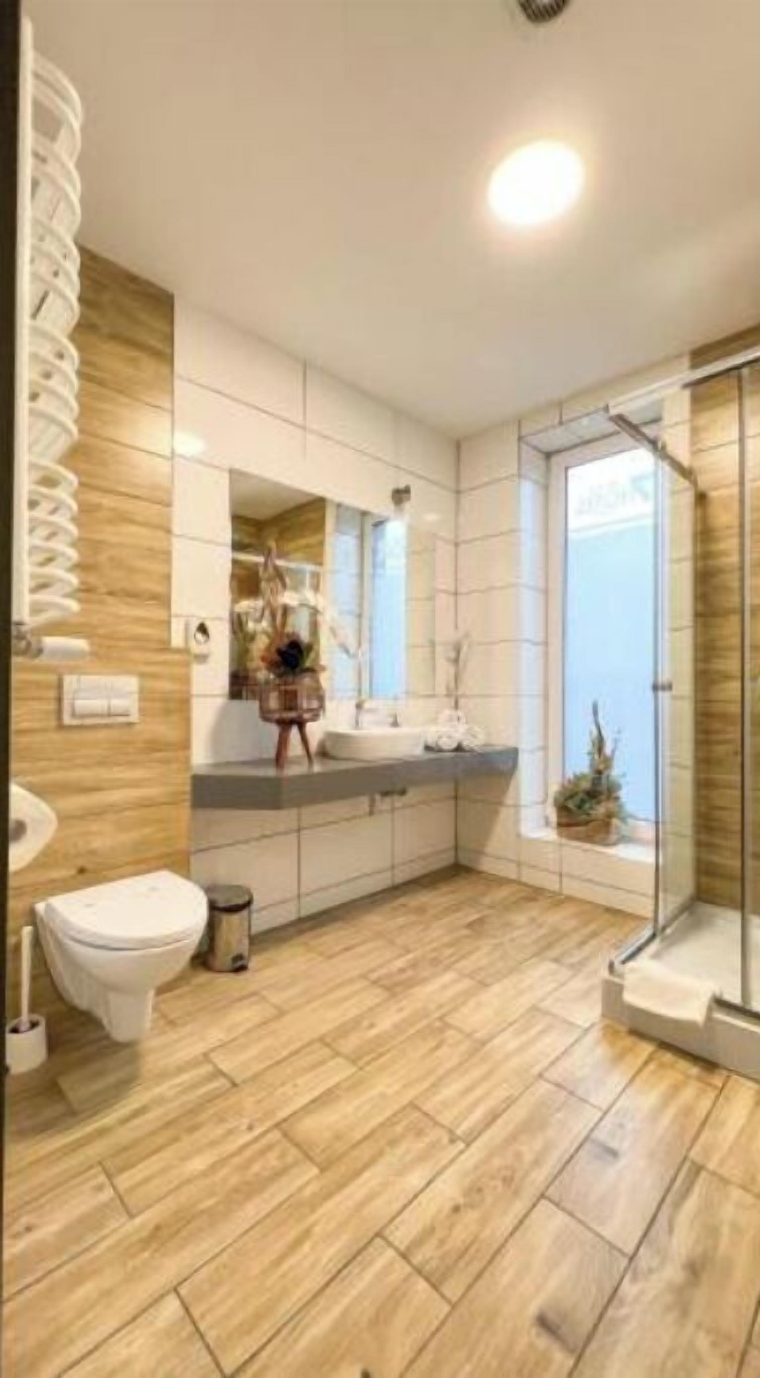 A modern bathroom with a wooden floor, a toilet, a sink, and a shower.