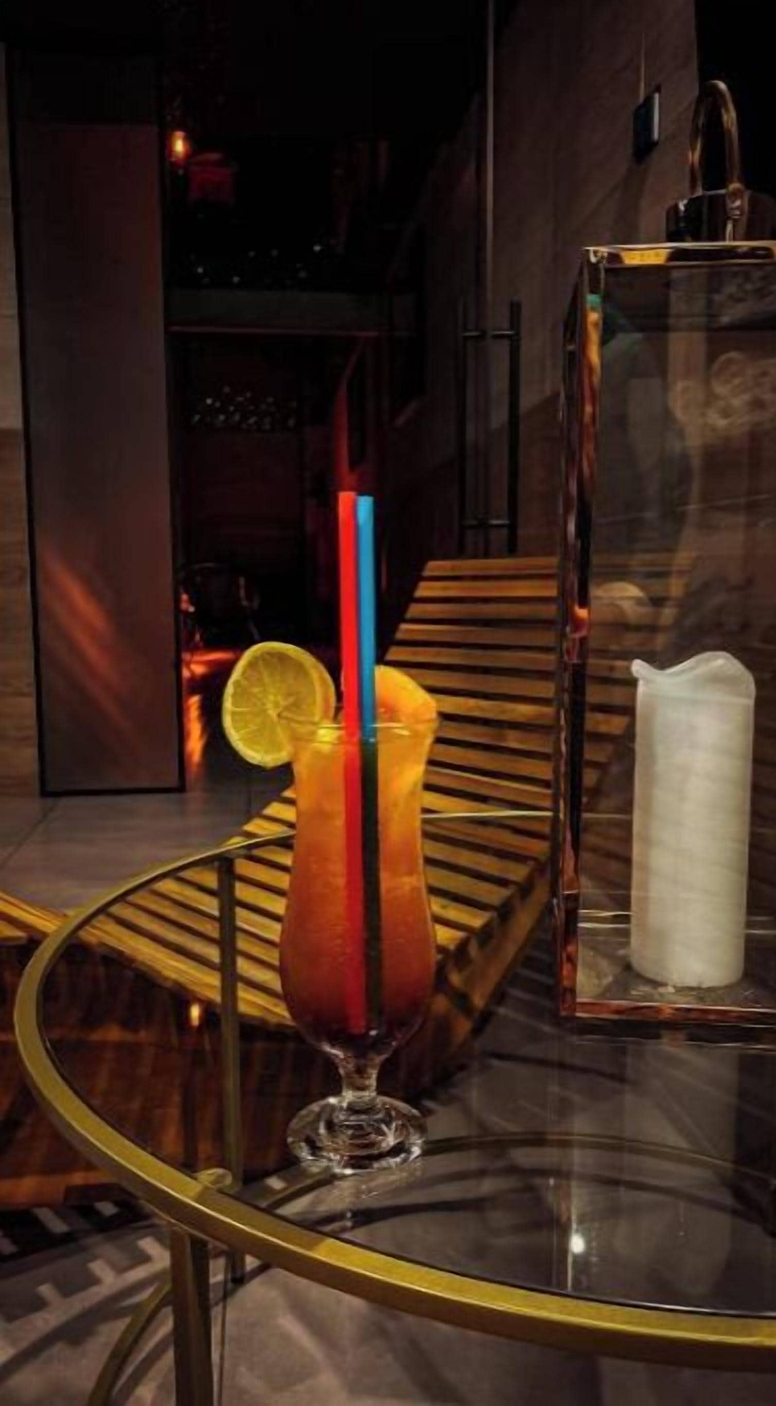 A glass table with a cocktail, a lemon slice, and a candle.