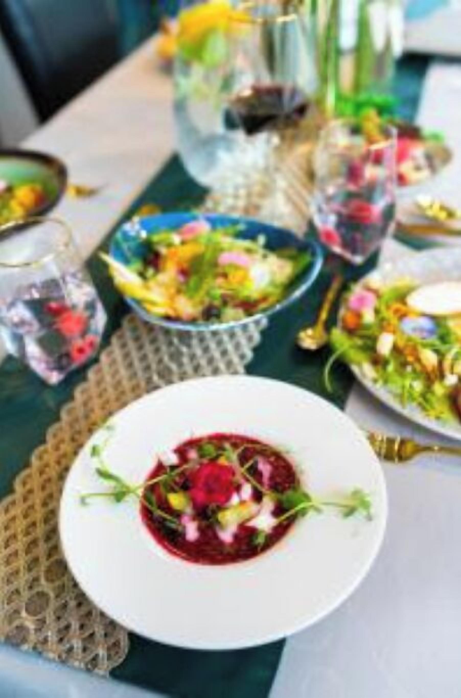 A dining table with various dishes, including a beetroot salad and a colorful salad, set on a tablecloth.