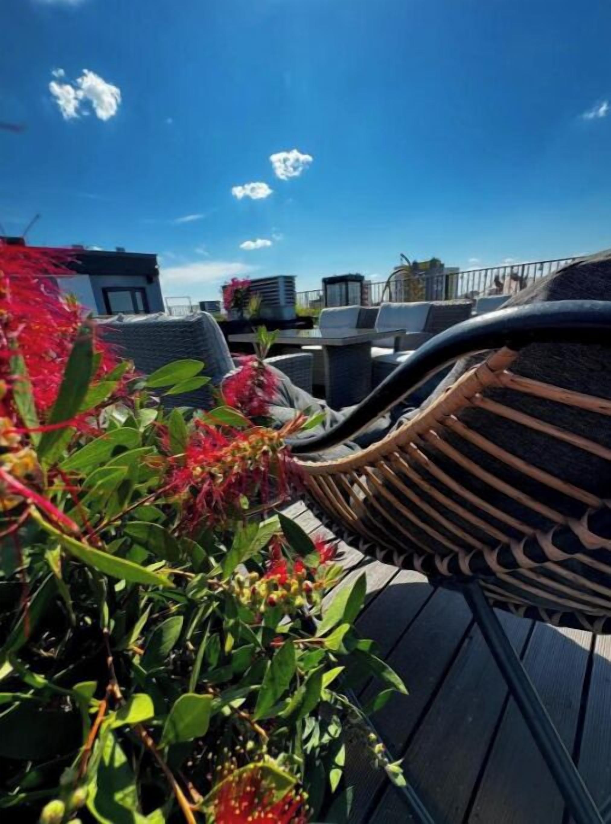 A rooftop terrace with outdoor seating, a view of the city skyline, and a clear blue sky.