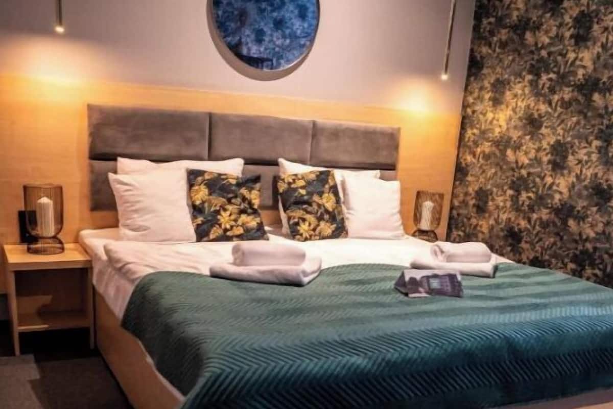 A bed with a green bedspread, two pillows, and a round mirror above it.
