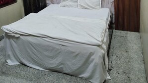 A bedroom with a bed, a ceiling fan, and a wooden headboard with a leaf pattern. - Shri Laddu Gopal Dham (Mathura)