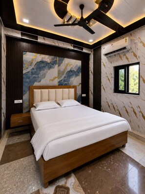 A modern bedroom with a bed, a ceiling fan, and a window. - Shri Laddu Gopal Dham (Mathura)