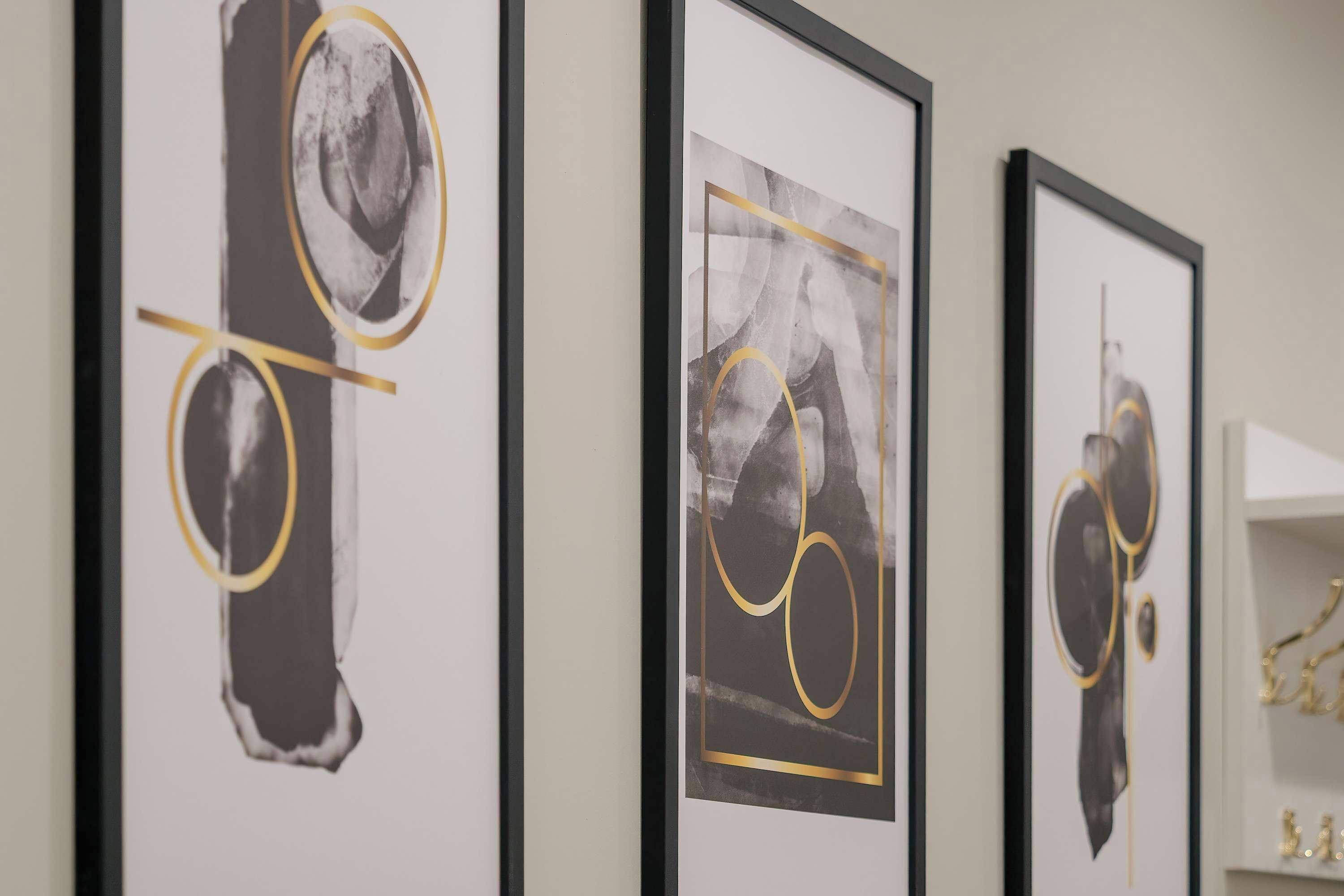 Three framed artworks with abstract designs and gold accents on a wall.