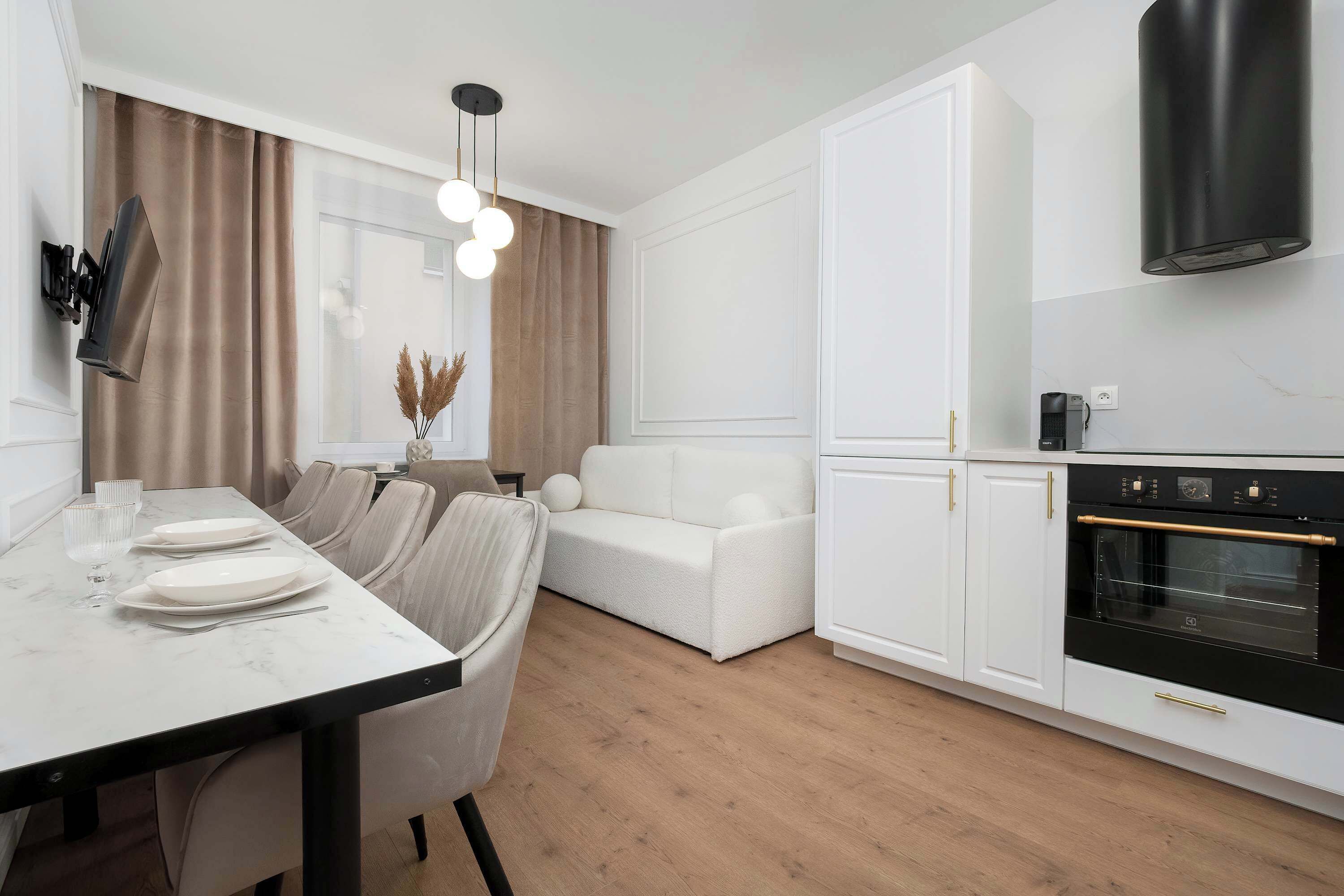 A modern kitchen with white cabinetry, a black oven, and a dining area with a marble table and white chairs.