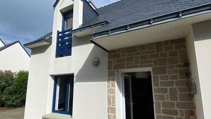 Ein modernes Haus mit einer Stein-Fassade, einer Holzterrasse und einem grauen Dach.