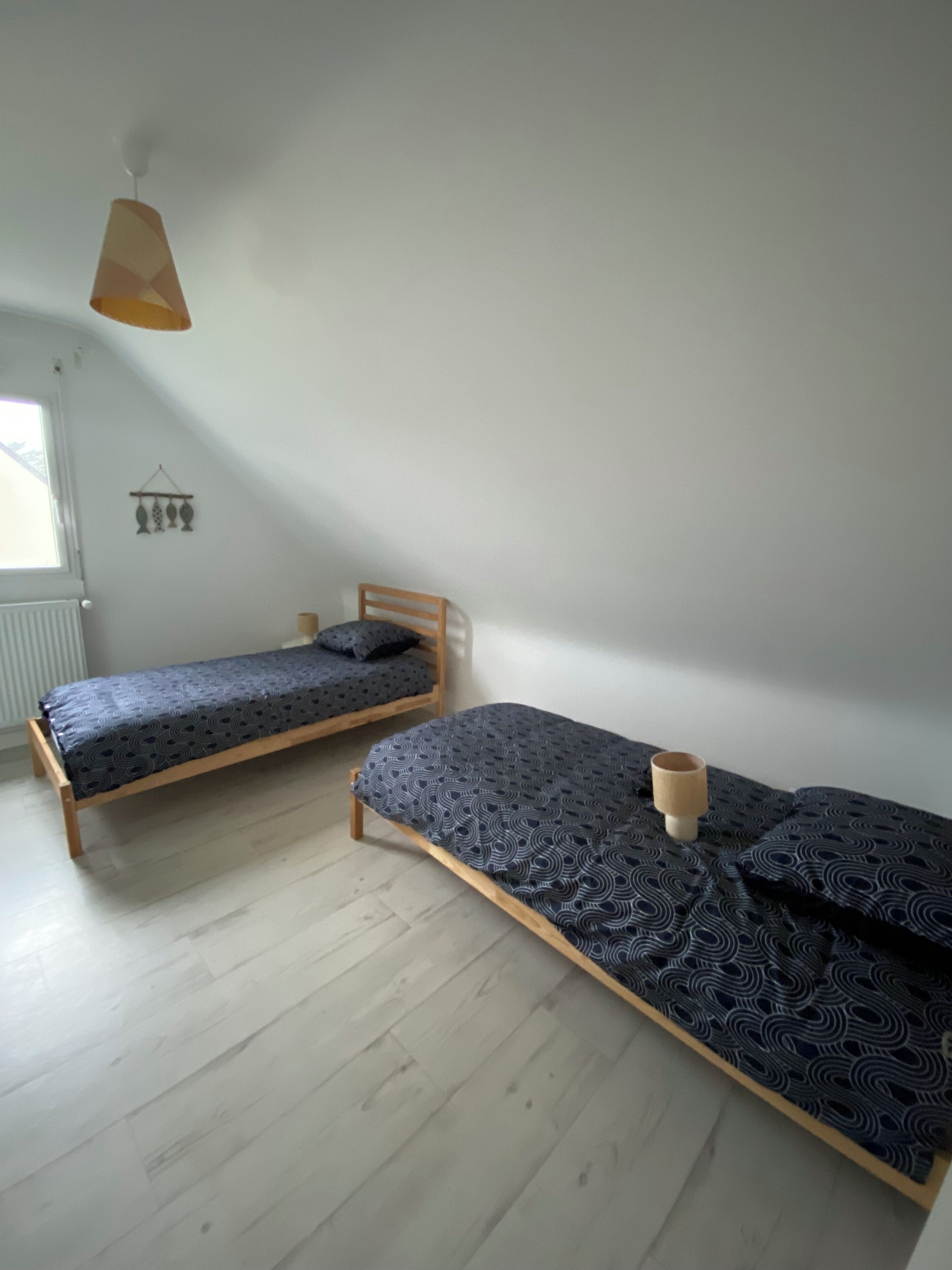 Une pièce avec deux lits en bois, un luminaire suspendu, un radiateur et une fenêtre.