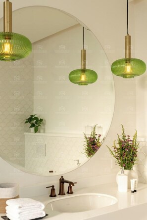 Een badkamer met een ronde spiegel, een wastafel en twee groene hanglampen.