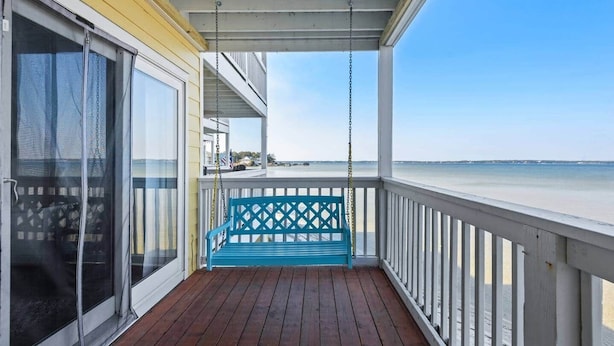Una terraza de madera con una silla colgante azul, un vidrio y vistas a la playa.
