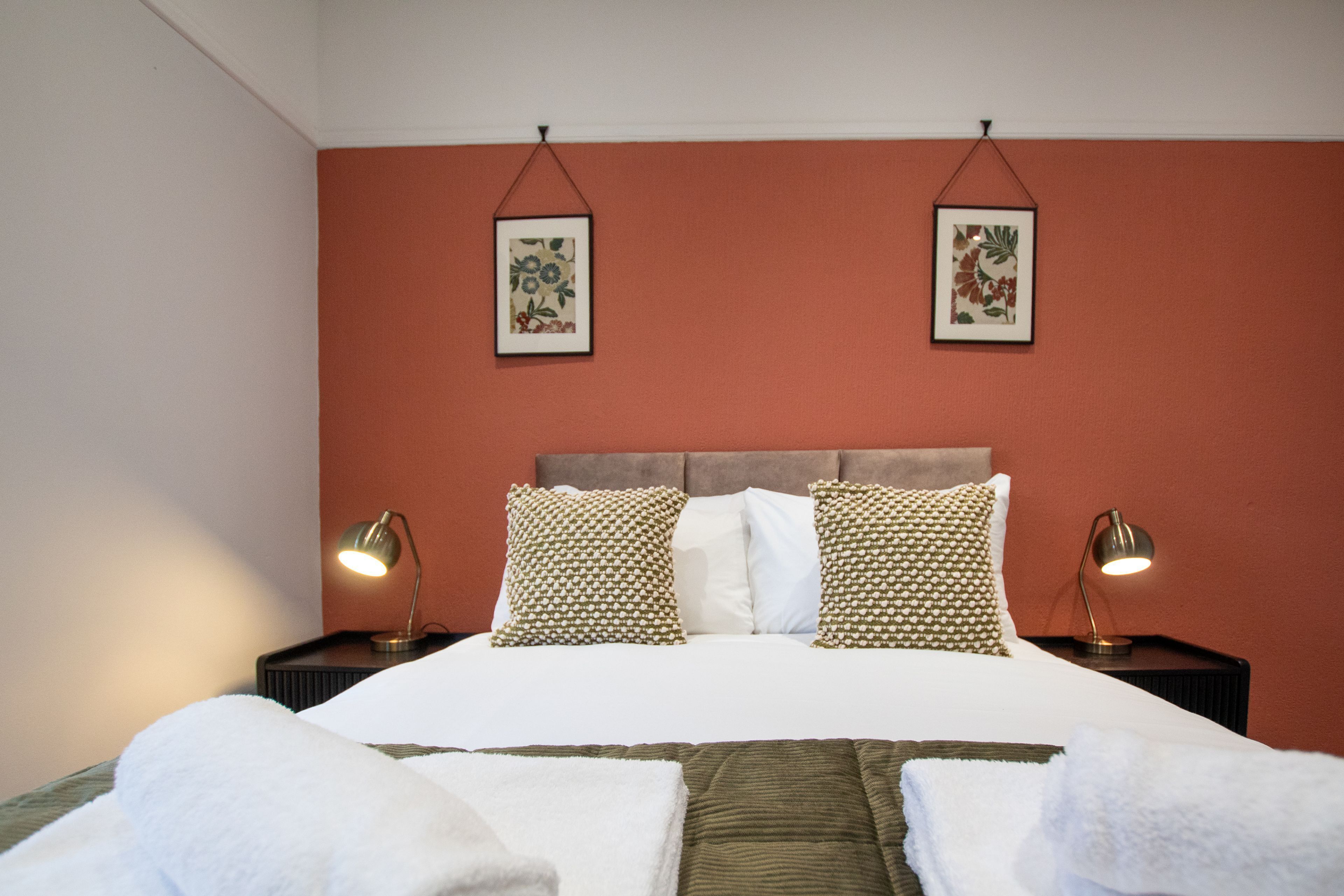 Ett hotellrum med en säng, två sänglampor och två inramade tavlor på väggen.