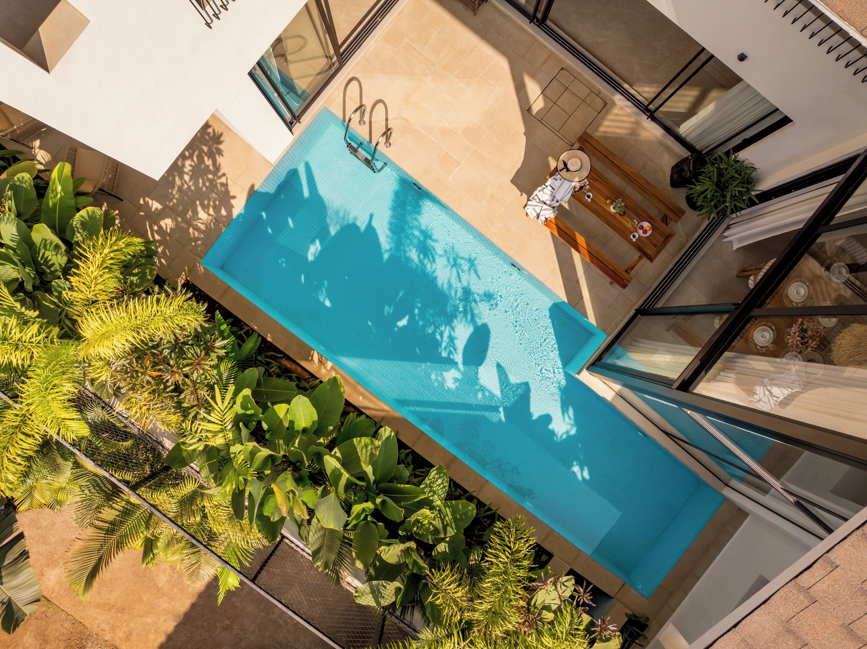 A rooftop pool with a glass enclosure, surrounded by lush tropical plants.