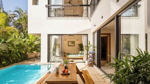 Ein modernes, zweistöckiges Haus mit Swimmingpool, einem Essbereich mit Tisch und Stühlen sowie einem Balkon mit Blick auf den Pool.