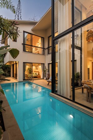 Une maison moderne dotée d’une piscine, de grandes baies vitrées et d’un balcon.