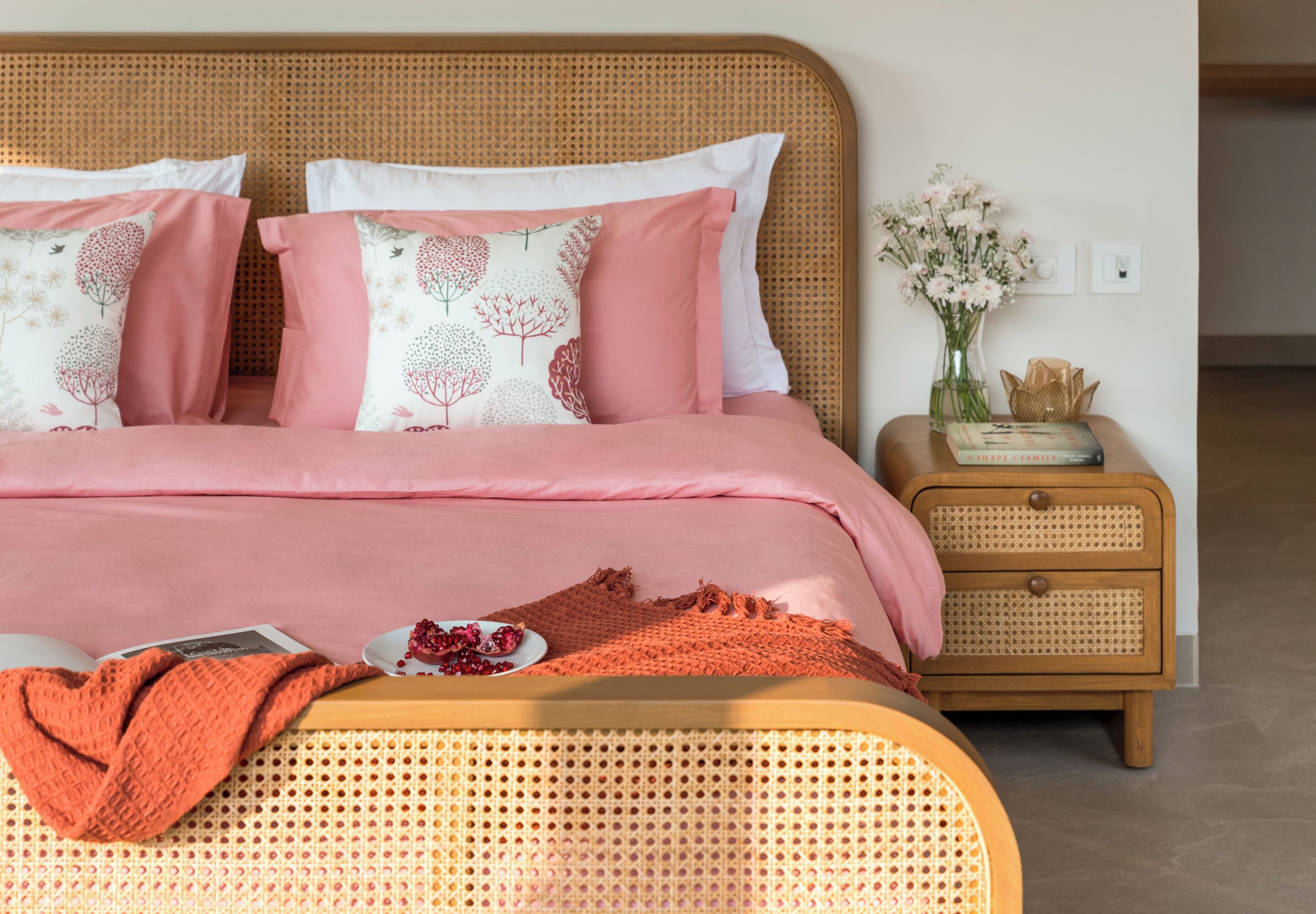 A bed with a woven headboard, a bedside table with a vase of flowers, and a small decorative box.