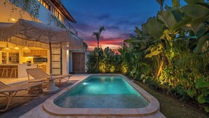A swimming pool with lounge chairs, a kitchen area, and lush tropical plants. - Sunbeam Oasis (Munggu)