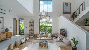 A spacious living area with a large sectional sofa, a coffee table, and a staircase leading to an upper level. - Sunbeam Oasis (Munggu)