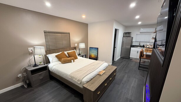 A modern bedroom with a large bed, bedside tables, a nightstand, a wall-mounted lamp, and a painting.