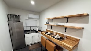 A compact kitchen with a refrigerator, microwave, and built-in oven. There is a wooden countertop with a sink and a chair.