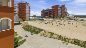 Et hotel med flere etager, et sandstrandområde med kaktusser og en klar blå himmel.