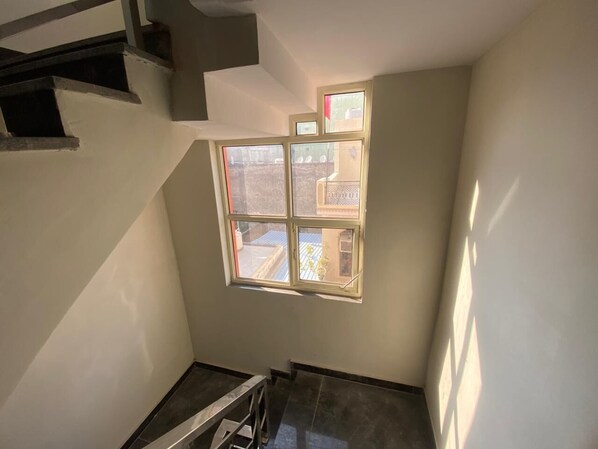 A stairwell with a window overlooking a courtyard. - Vansh Residency Couple Friendly Gurgaon (Gurugram)
