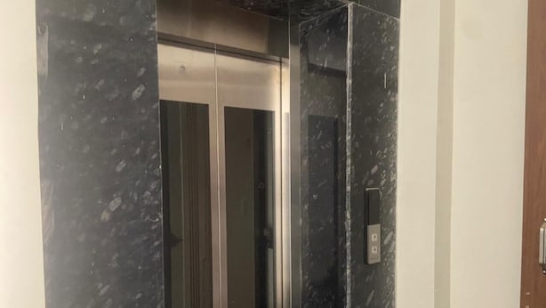 Un ascenseur avec un intérieur métallique et un mur en marbre.