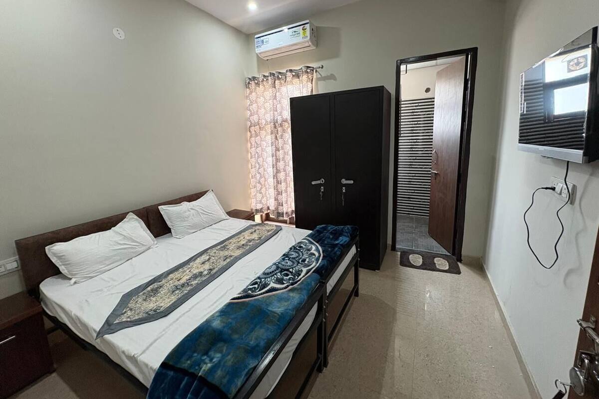A bedroom with a bed, a wardrobe, a television, and an air conditioning unit.