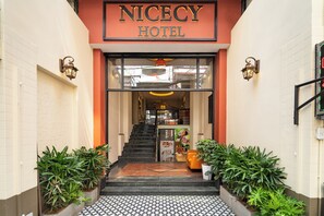 La entrada al Hotel Nicecy, con suelo de baldosas, una escalera y plantas en macetas.