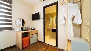 A compact hotel room with a wooden floor, a small desk with a mirror, a TV, a mini fridge, and a shower area. - Nicecy Hotel - Bui Vien Central (Ho Chi Minh City)