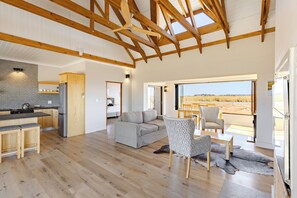 A spacious living area with a wooden ceiling, a grey sofa, a patterned armchair, and a view of the outdoors. - Quagga Lodge (Velddrif)