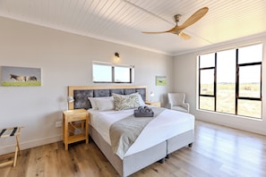 A bedroom with a bed, nightstand, chair, and large windows.