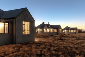 A row of modern, single-story houses with large windows and a flat roof, set in a grassy field. - Quagga Lodge (Velddrif)