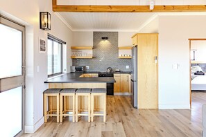 A modern kitchen with a central island, wooden bar stools, and a brick backsplash. - Quagga Lodge (Velddrif)