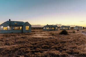 A row of modern houses with large windows, set in a grassy field with a clear sky. - Quagga Lodge (Velddrif)