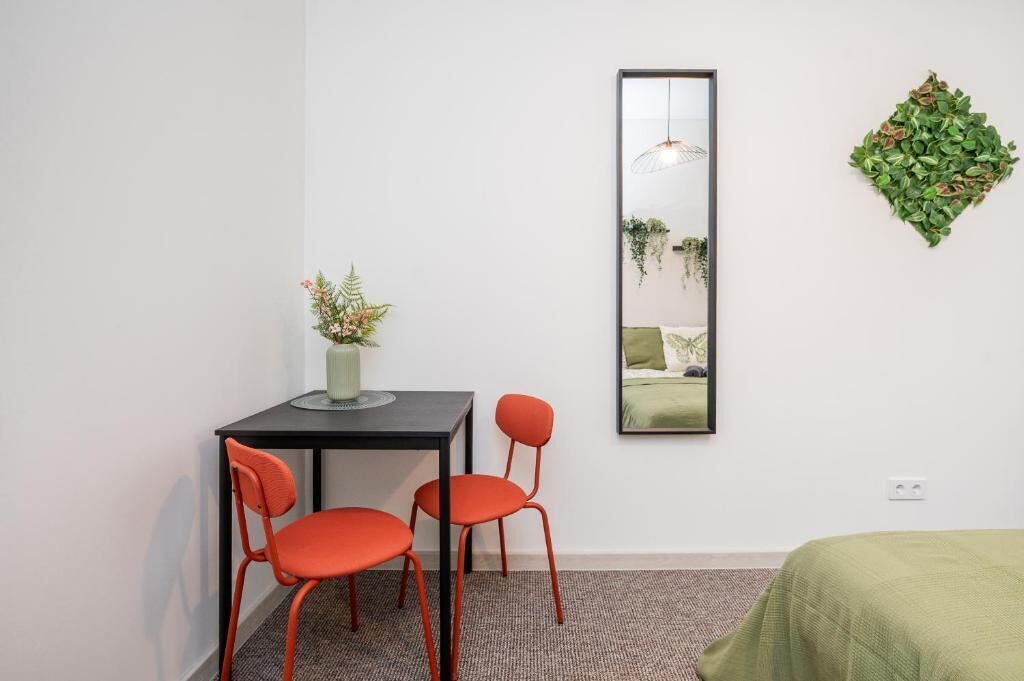 Une pièce comprenant un lit, un bureau avec deux chaises, un miroir et une plante fixée au mur.