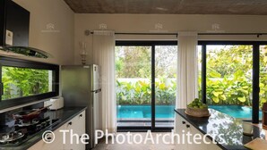 A modern kitchen with a built-in stove, a refrigerator, and a large window overlooking a swimming pool. - TBK VILLA ASSAGAO ZEN (Assagao)