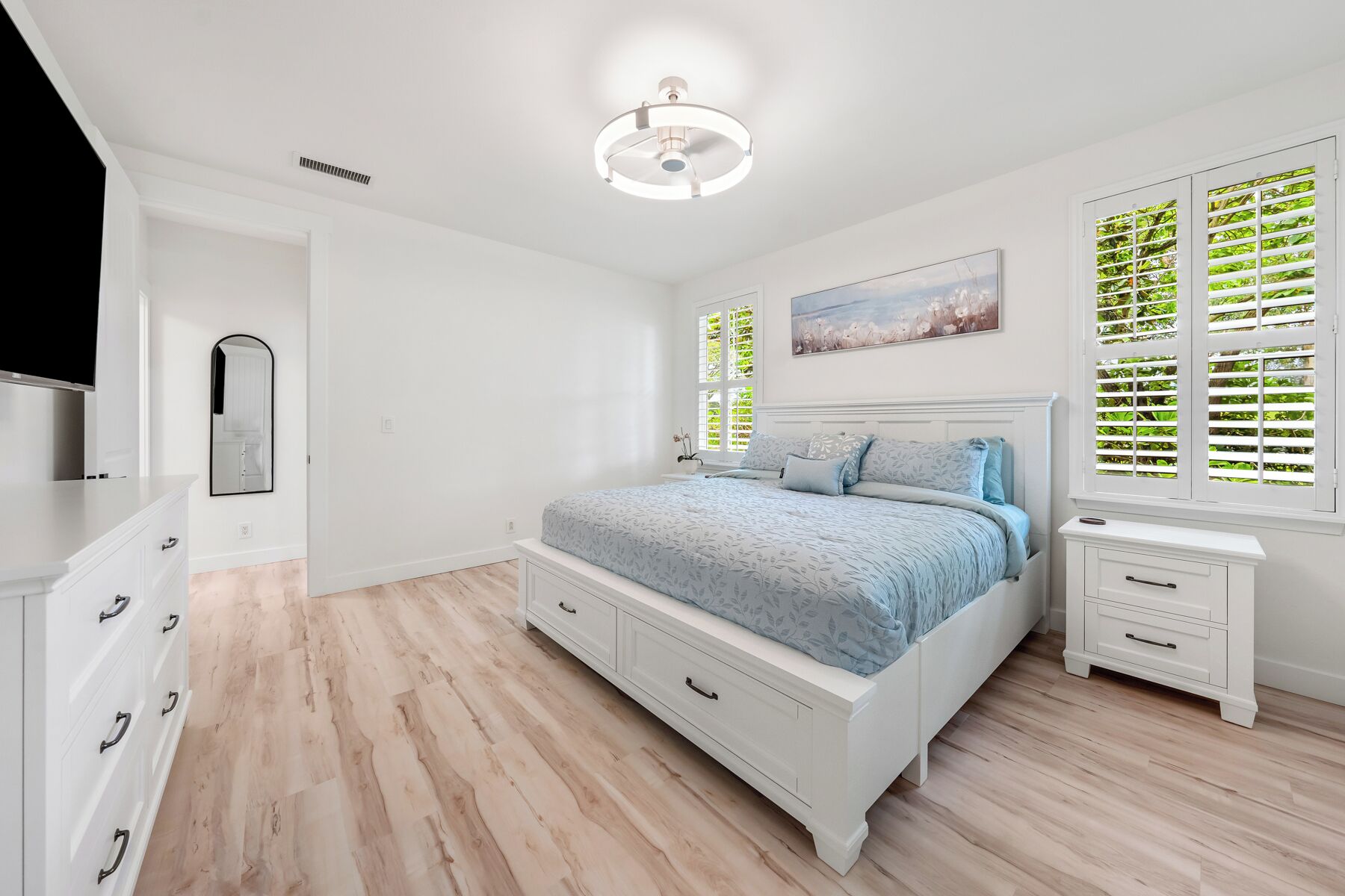 A bedroom with a bed, bedside tables, a mirror, and a ceiling light fixture.