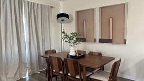 Ein Essbereich mit einem Holztisch, Stühlen, einer Stehlampe und zwei gerahmten Kunstwerken an der Wand.