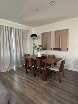 A dining area with a wooden table and chairs, a floor lamp, and two framed artworks on the wall. - Moreno Valley Retreat / Lake Perris & UC Riverside (Moreno Valley)