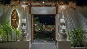 Entrada de hotel con techo de paja, dos grandes estatuas de piedra y un letrero que dice 'ETHICA'.