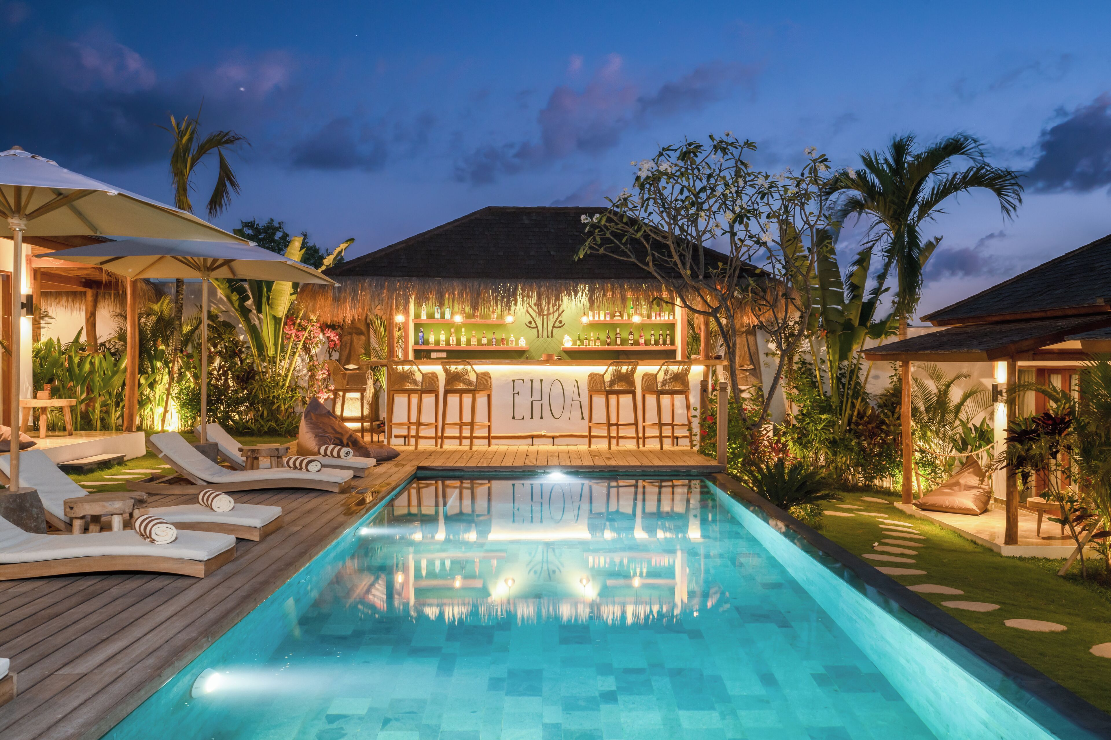 A pool area with lounge chairs, a bar, and tropical plants.