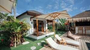 Un resort tropical con terraza de madera, sillas de descanso y un área de bar con techo de paja.